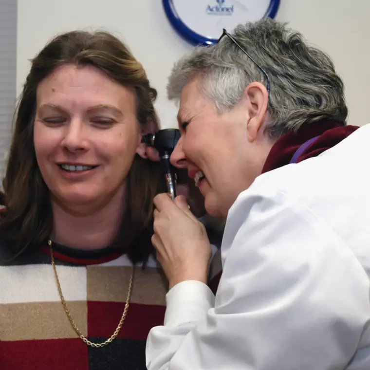 Doctor examining a smiling patient's ear with an otoscope